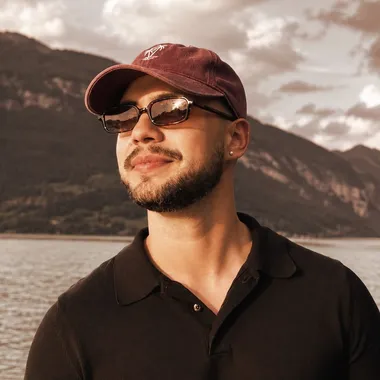 Nestor Peña in a cap and sunglasses by a mountain lake