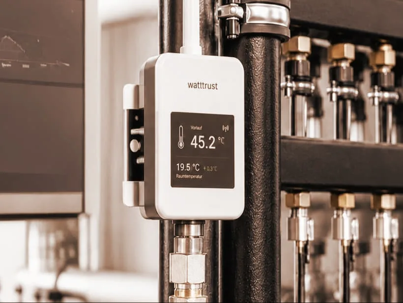 An ECCO2 sensor mounted on heating pipes, its display showing the water temperature
